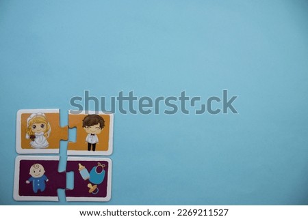 Colorfully colored jigsaw puzzle pieces with pictures of bride, groom, baby and baby tools placed side by side on the lower left side of a blue background.
