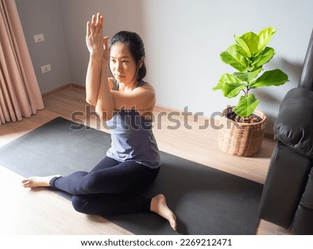 seated eagle pose yoga sitting Garudasana asian woman home workout fitness body exercise pilates health training healthy lifestyle activity wellness care on mat indoors natural light selective focus