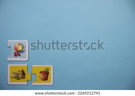 Colorfully colored puzzle pieces with pictures of a pile set, a pile ball and a sand bucket placed on the lower left of a blue background.