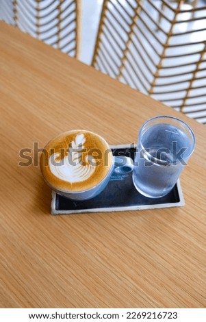 Blue cup of tasty cappuccino with beautiful latte art and glass of water on wooden table background