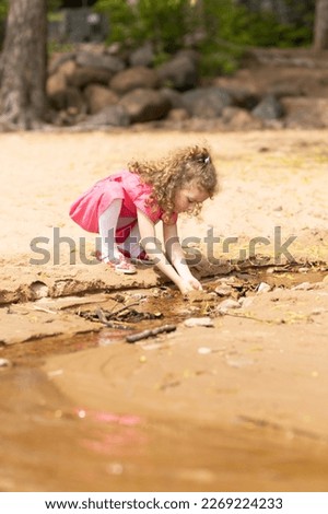 little cute pensive curly girl playing next to the water in the sand, breathing fresh air in nature. concept of spring, summer, travel, childhood. Child enjoying freedom, relaxation