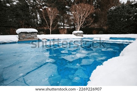 Pool with ice and slush after snow storm. Inground pool with pool cover and ice layer in backyard with deep snow. Winterizing pool for cold, freezing or sub zero temperature. Selective focus. Royalty-Free Stock Photo #2269226907