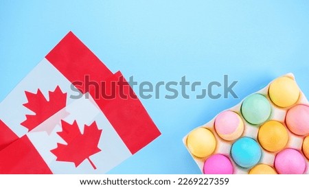 Colorful Easter eggs pack and two canadian flags on blue background with space for text. Spring flat lay. Pastel painted eggs in box