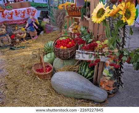 Various vegetables and fruits are offered for sale at the fair: pumpkins, zucchini, tomatoes, apples. There are funny figurines nearby. Harvest festival. Bright colors of autumn decor set outdoors.