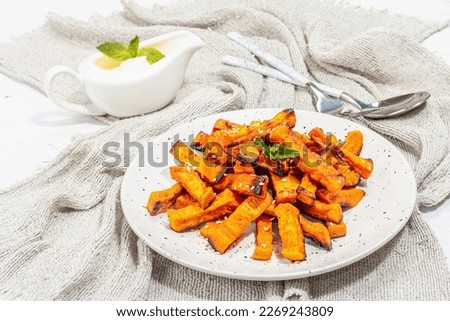 Baked organic batata fries with spices and sauce. Sweet vegetable, served portion and cutlery, ready-to-eat vegan food. White plaster background, copy space