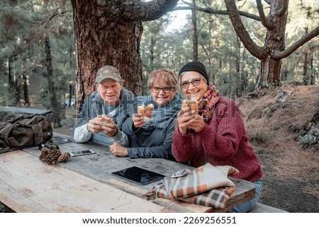 Group of smiling friends or family sitting in outdoors at wooden table in pic nic area in the woods ready to eat their sandwiches