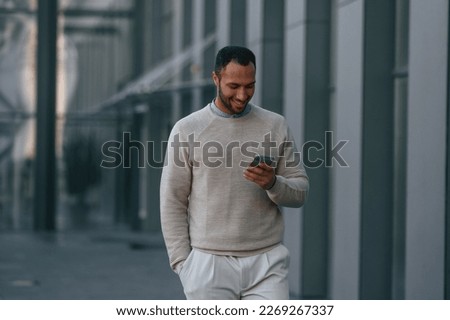 Handsome man is walking, holding smartphone. Outdoors near the business building.