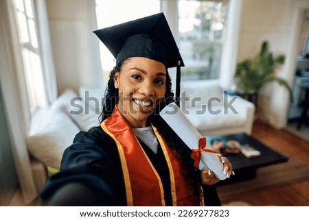 Happy African American graduate student taking selfie after receiving university certificate.