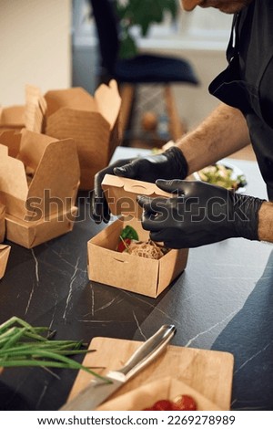 Fresh burger with vegetables. Man is packing food into the paper eco boxes. Indoors, restaurant.