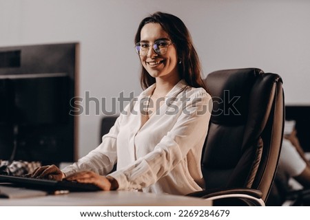 Smiling girl in glasses working in office. Beautiful receptionist woman typing on computer keyboard