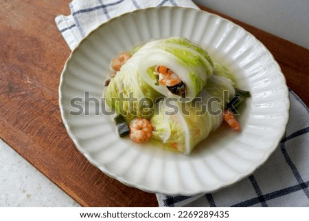 Chinese cabbage rolls with shrimp, shiitake mushroom, carrots and noodles. Stewed with stock. On a white plate.Wooden table.
