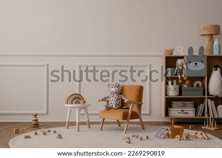 Minimalist composition of kid room interior with copy space, orange armchair, wooden sideboard, round stool, beige rug plush toys, wooden blockers ant personal accessories. Home decor. Template.