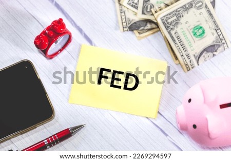 The acronym FED written on a piece of paper lying on a wooden table. Bills of dollars and a piggy bank in the composition. Economy and investments.
