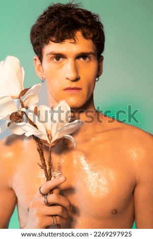 Portrait of shirtless man with oil on skin holding magnolia branch on green background
