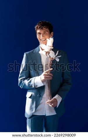 Stylish man in suit and shirt holding magnolia branch isolated on navy blue