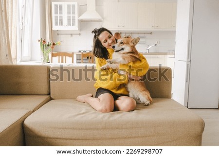 A brunet girl in a yellow sweater hugs a dog sitting on the couch . High quality photo