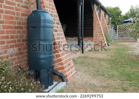 green rainwater tank or water butt connected to a rain collector at the side of a converted barn Royalty-Free Stock Photo #2269299753
