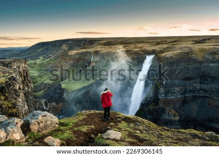 Majestic Haifoss waterfall flowing in volcanic canyon and traveler taking a picture among the Icelandic Highlands in summer at Iceland