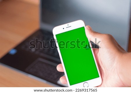 Hand hold smartphone green screen on wooden background.