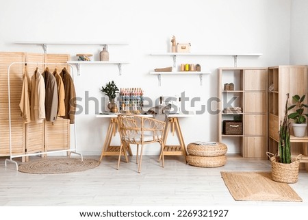 Interior of modern atelier with tailor's workplace, clothes and shelves