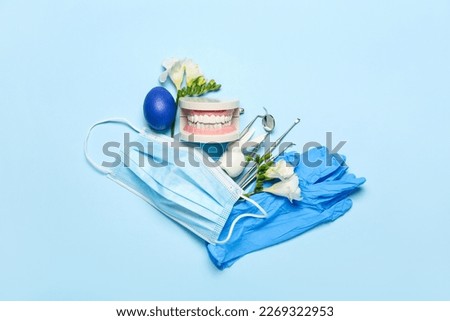 Dental tools with jaw model, flowers and Easter egg on blue background