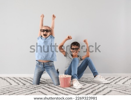 Little boy and his sister in 3D glasses watching cartoons on TV near light wall