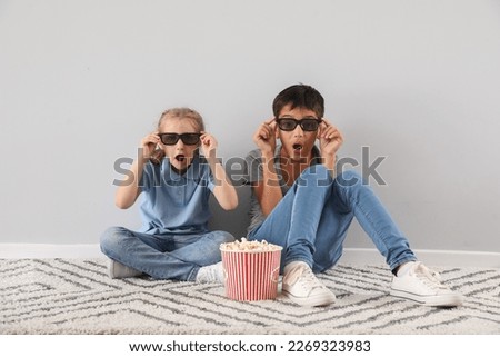 Shocked little boy and his sister in 3D glasses watching cartoons on TV near light wall