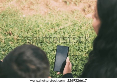view from the back group of laughing Latinos sitting on the ground in a park with a smartphone