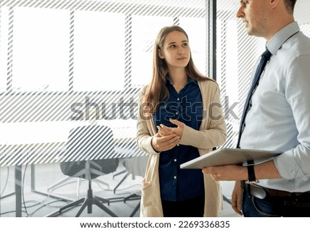 Businesswoman communicates and discuss business project with male colleague while standing in the modern office after meeting. Female manager talking, and brainstorming with success corporate team