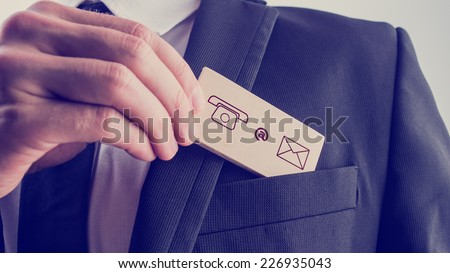 Businessman removing a wooden card with contact icons from the pocket of his suit jacket, vintage effect toned image.