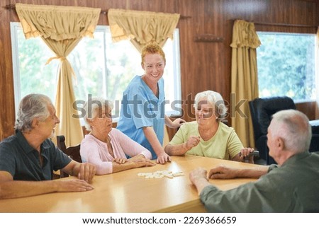 Group of seniors with dementia sitting at a table playing dominoes under the guidance of a geriatric nurse