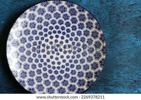 Blue ceramic plate with beautiful pattern. Dark blue textured background with copy space. Modern tableware close up photo. 
