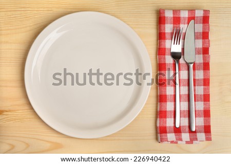Empty plate with cutlery on red checkered napkin on wooden background.