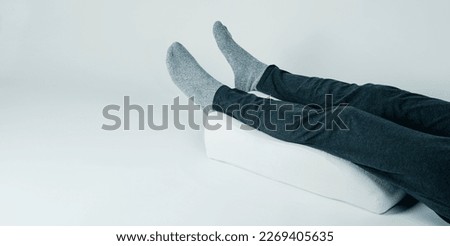 closeup of a man using a leg elevation pillow, made of memory foam, laying on a white background, in a panoramic format to use as web banner Royalty-Free Stock Photo #2269405635