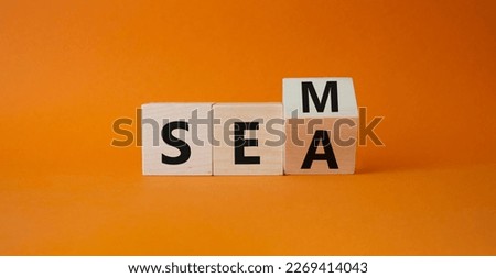 SEM vs SEA symbol. Turned wooden cubes with words SEA and SEM. Beautiful orange background. Business and SEM vs SEA concept. Copy space