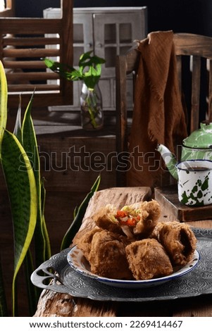 (Tahu mercon)  is tofu which contains vegetables and chilies inside, placed on a plate on a tray served with tea in a green glass and its teapot, with a traditional wooden nuance background.