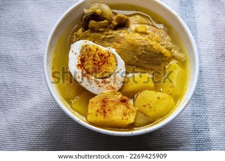 Chicken soup with potatoes and egg on top, served on a wooden table...