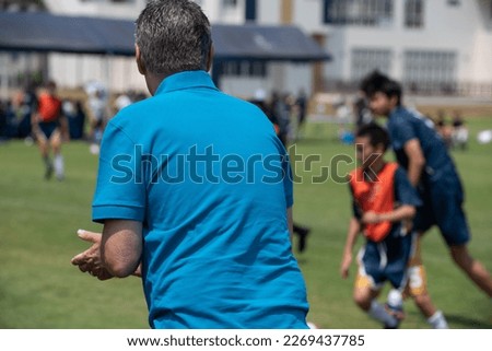 Soccer dad standing and watching his son playing football in a school tournament on a clear sky and sunny day. Sport, outdoor active, lifestyle, happy family and soccer mom  soccer dad concept. Royalty-Free Stock Photo #2269437785