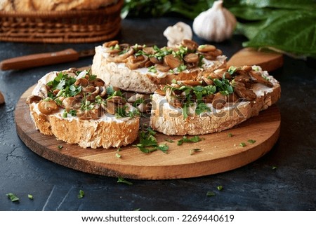 Beautiful appetizing bruschetta cream cheese and fried champignon mushrooms. Garnished with fresh herbs on a wooden cutting board. Royalty-Free Stock Photo #2269440619