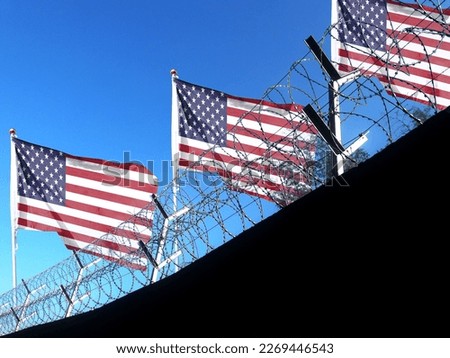 The American flag hangs in the cloudy sky outside the prison's barbed wire. waving in the sky
