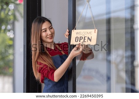Asian woman is a waitress in an apron, the owner of the cafe stands at the door with a sign Open waiting for customers. SME Small business concept, cafes and restaurants 