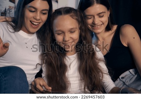      Staged photo. Lesbian couple and their kids are having a good time at home. Cozy atmosphere. One of the girls is looking at a picture book with her parents. They are all laughing.                