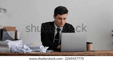 Perplexed, puzzled handsome businessman looking at laptop screen at workplace in office. Young CEO or project manager is not sure whether he should agree to the deal, sign contract, buy stock shares.
