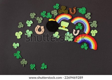 St Patrick's Day concept. Knitted composition of a green hat, a pot of gold, a horseshoe, a rainbow and green shamrocks on a black background