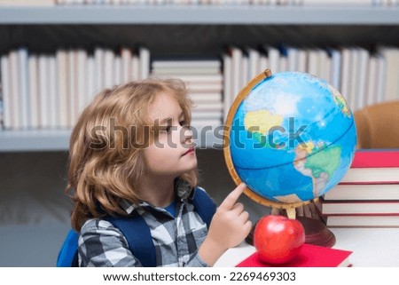 Pupil looking at globe in library at the elementary school. Nerd school kid. Clever child from elementary school with book. Smart genius intelligence kid ready to learn. World globe. Royalty-Free Stock Photo #2269469303