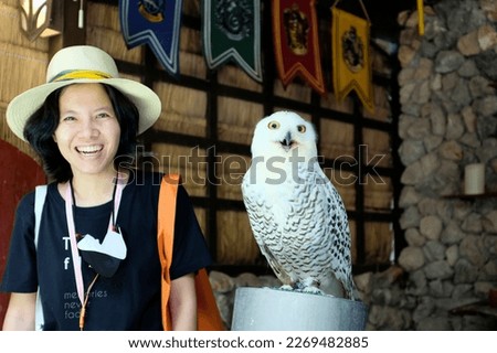 An Asian female tourist playing with a large white snowy owl at a zoo in Kanchanaburi, Thailand.