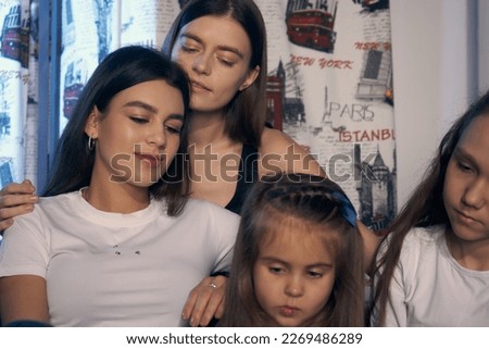     Staged photo. Lesbian couple and their kids are having a good time at home.  Parents and girls nestled on the couch close to each other. There is love and happiness on their faces.                