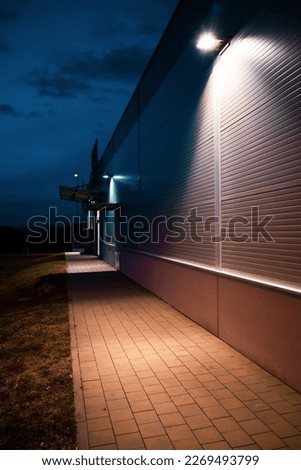 Illuminated industrial building in the evening Pavement and grass. Royalty-Free Stock Photo #2269493799