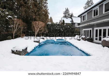Pool with ice and slush after snow storm. Inground pool with pool cover and ice layer in backyard with deep snow. Winterizing pool for cold, freezing or sub zero temperature. Selective focus. Royalty-Free Stock Photo #2269494847