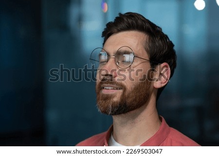Close-up photo. A young calm man in glasses and a red shirt sits in the office, closes his eyes, rests, meditates, thinks, dreams.